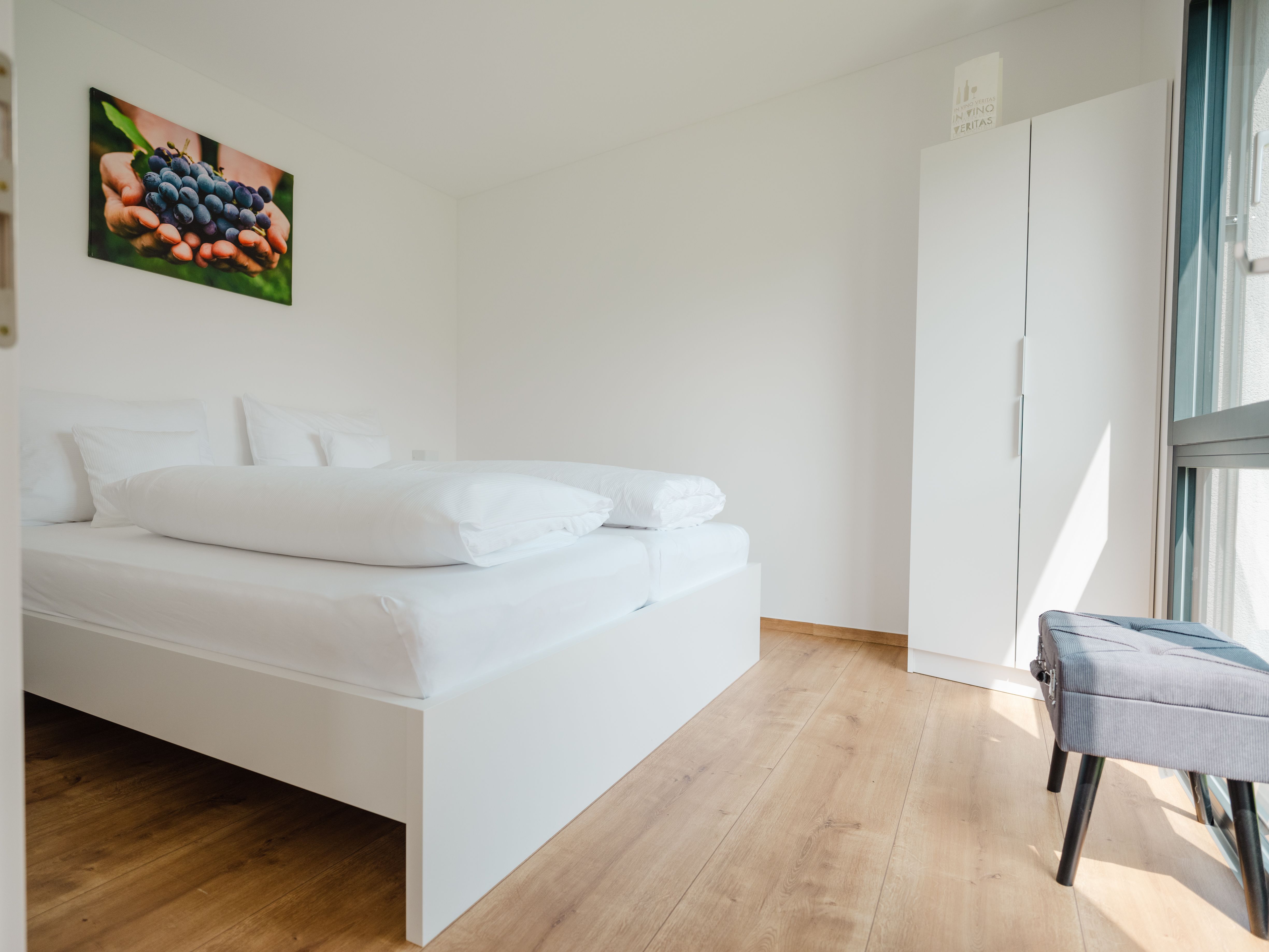 Modernes Schlafzimmer mit weißem Bett, Holzfußboden und Bild von Trauben an der Wand.