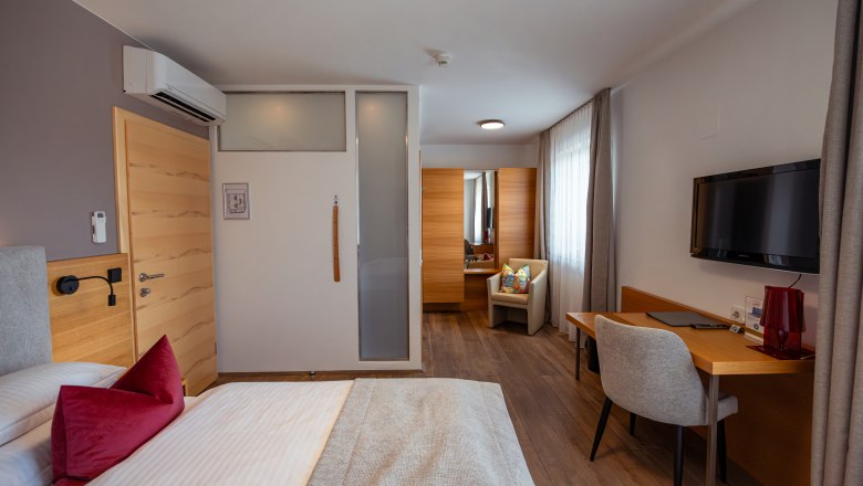 Modern eingerichtetes Hotelzimmer mit Bett, Schreibtisch, Stuhl und Fernseher.