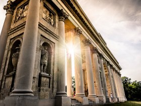 Die majest&auml;tische Raistenkollonade strahlt im warmen Licht der Abendsonne und l&auml;dt dazu ein, die beeindruckende Architektur zu bewundern. Umgeben von &uuml;ppigem Gr&uuml;n und sanften H&uuml;geln, bietet dieser Ort eine perfekte Kulisse f&uuml;r entspannte Spazierg&auml;nge und unvergessliche Erinnerungen.