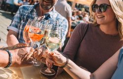 Lächelnde Personen stoßen bei Sonnenschein mit Weinviertler Wein in einer Innenstadt an. 