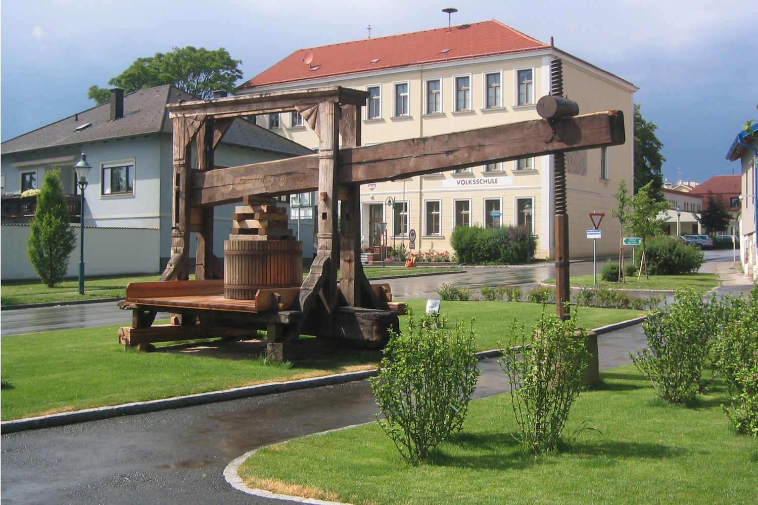 Historische Baumpresse vor einem Schulgebäude in einer grünen Umgebung.