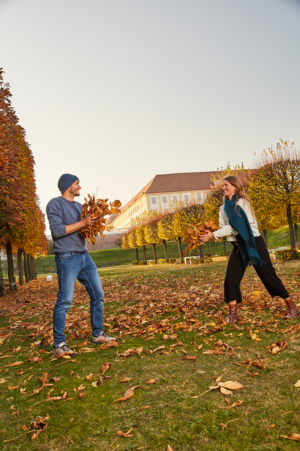 In der malerischen Kulisse von Schloss Hof genießen zwei Freunde einen fröhlichen Moment im bunten Herbstlaub. Die goldenen Blätter fallen sanft zu Boden, während sie sich spielerisch mit den Laubhaufen umgeben. Diese entspannte Atmosphäre lädt dazu ein, die Schönheit der Natur und die Freude an der Freundschaft zu erleben.