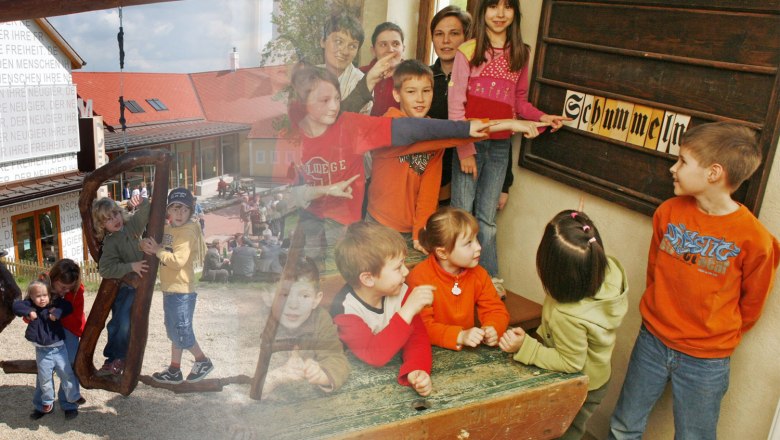 Kinder spielen im Freien und zeigen auf ein Schild mit der Aufschrift 'Schummeln'.