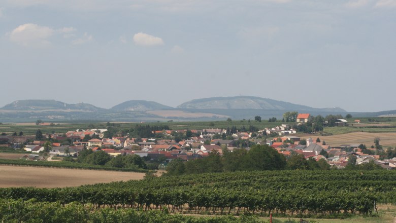 Landschaft mit Dorf, Weinbergen und Hügeln im Hintergrund.