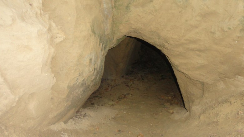 Eingang zu einer kleinen Höhle in sandigem Gestein.