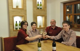 Vier Personen sto&szlig;en mit Weingl&auml;sern an einem Tisch an.