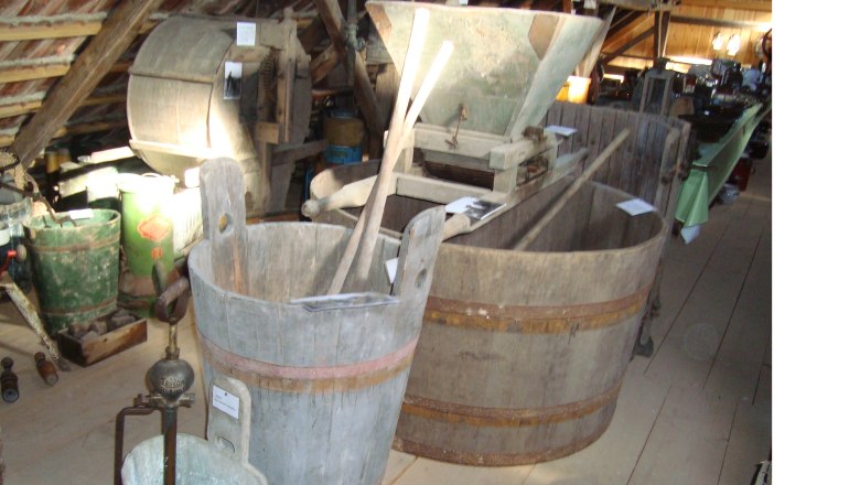 Innenansicht eines Museums mit alten landwirtschaftlichen Geräten und Holzbottichen.