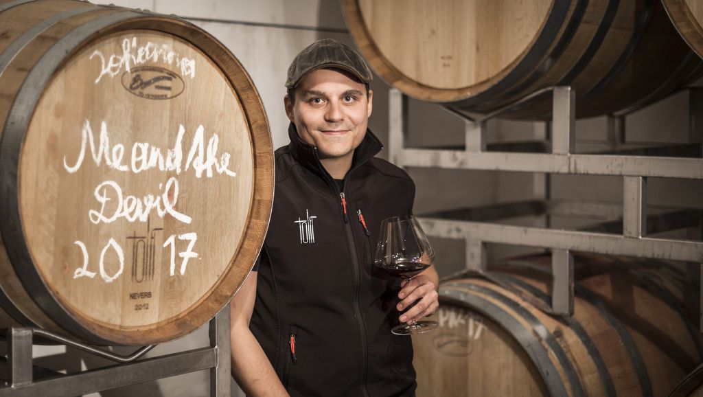Person in wine cellar with wine glass in front of wooden barrels.