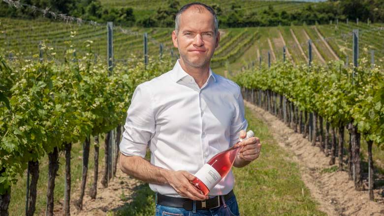 Mann in einem Weinberg hält eine Flasche Roséwein.