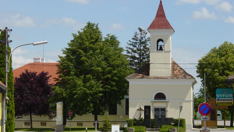 Kleine Kirche mit Glockenturm und rotem Dach, umgeben von Bäumen und Straßenschildern.