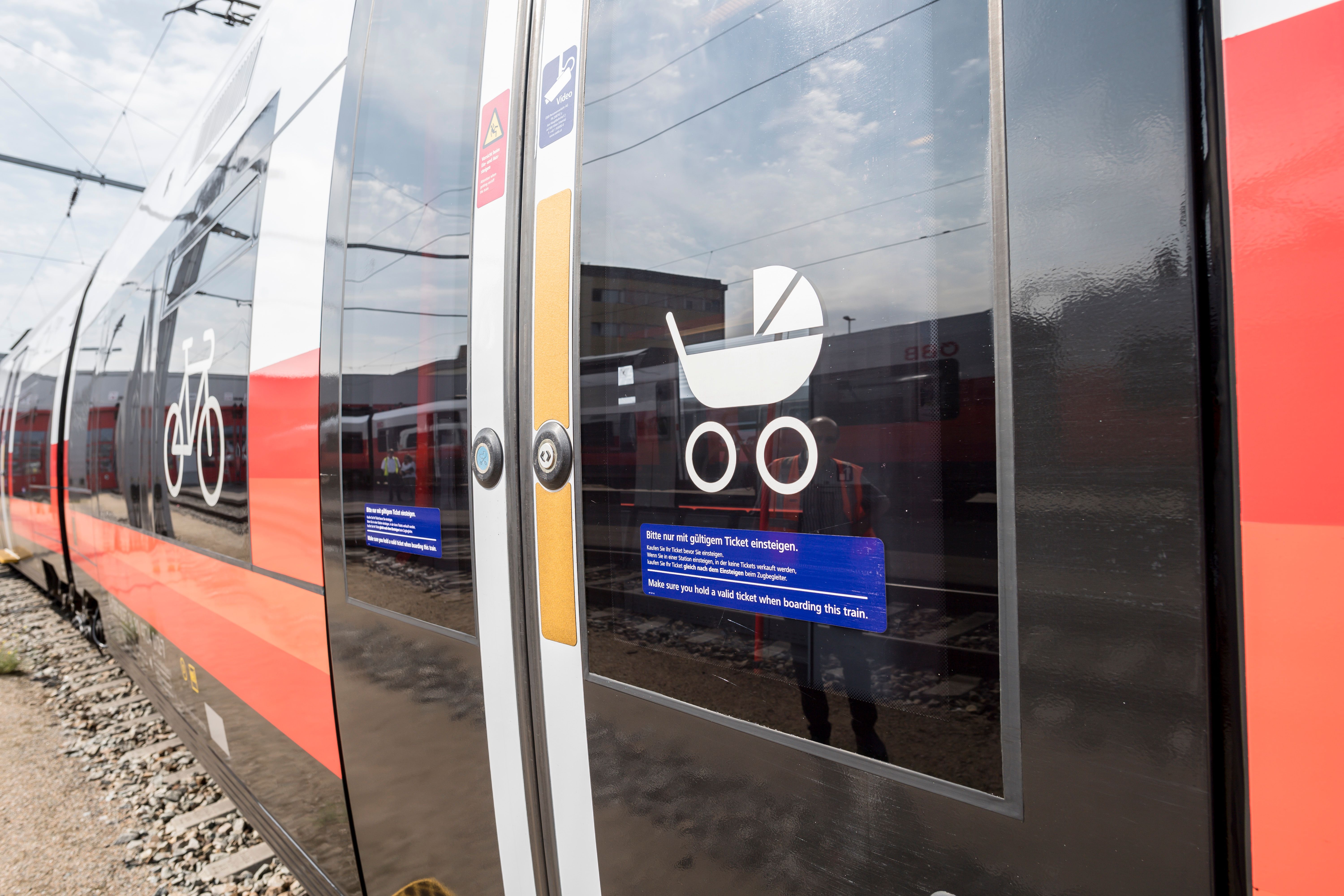Close-up of a train door with symbols for bicycles and baby carriages. Other trains and a building can be seen in the background.