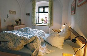 Gemütliches Schlafzimmer mit ungemachtem Bett und Blick aus dem Fenster auf eine Person mit Blumen.