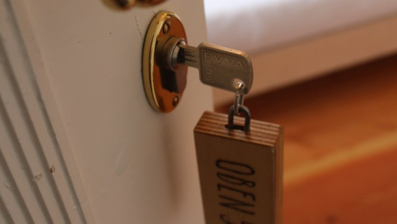 Nahaufnahme eines Türgriffs mit Schlüssel und Holzanhänger mit der Aufschrift 'OBEN 5'.