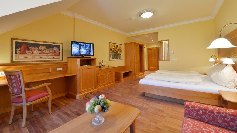 A cozy guest room with wooden furniture, a double bed, a desk, a TV and a plate of fruit on the table.
