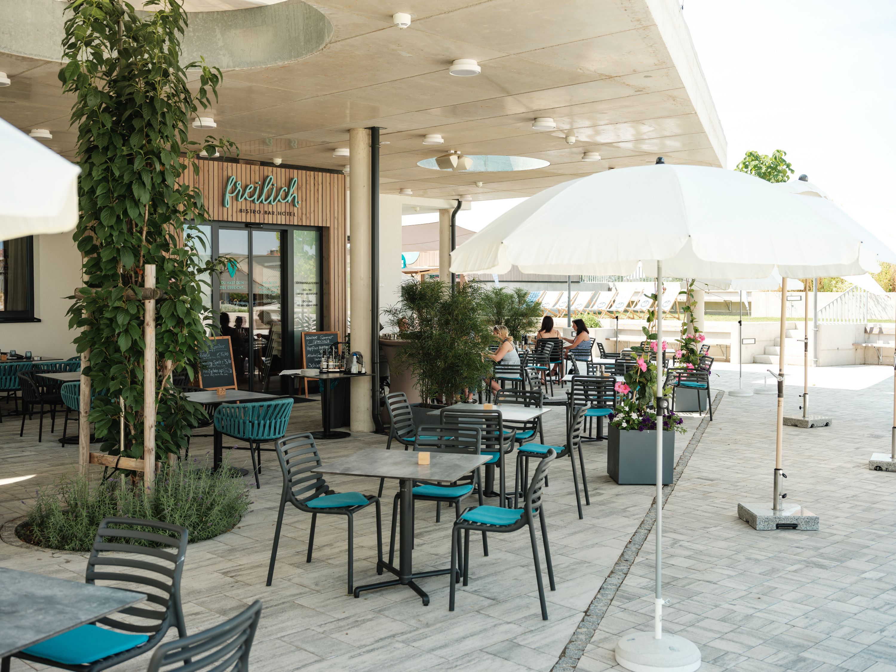 Außenbereich eines Cafés mit Tischen, Stühlen und Sonnenschirmen.