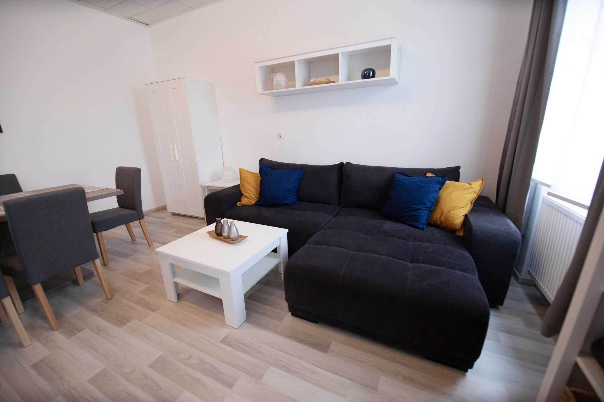 Moderner Wohnbereich mit grauem Sofa, bunten Kissen, weißem Couchtisch und Esstisch mit Stühlen.