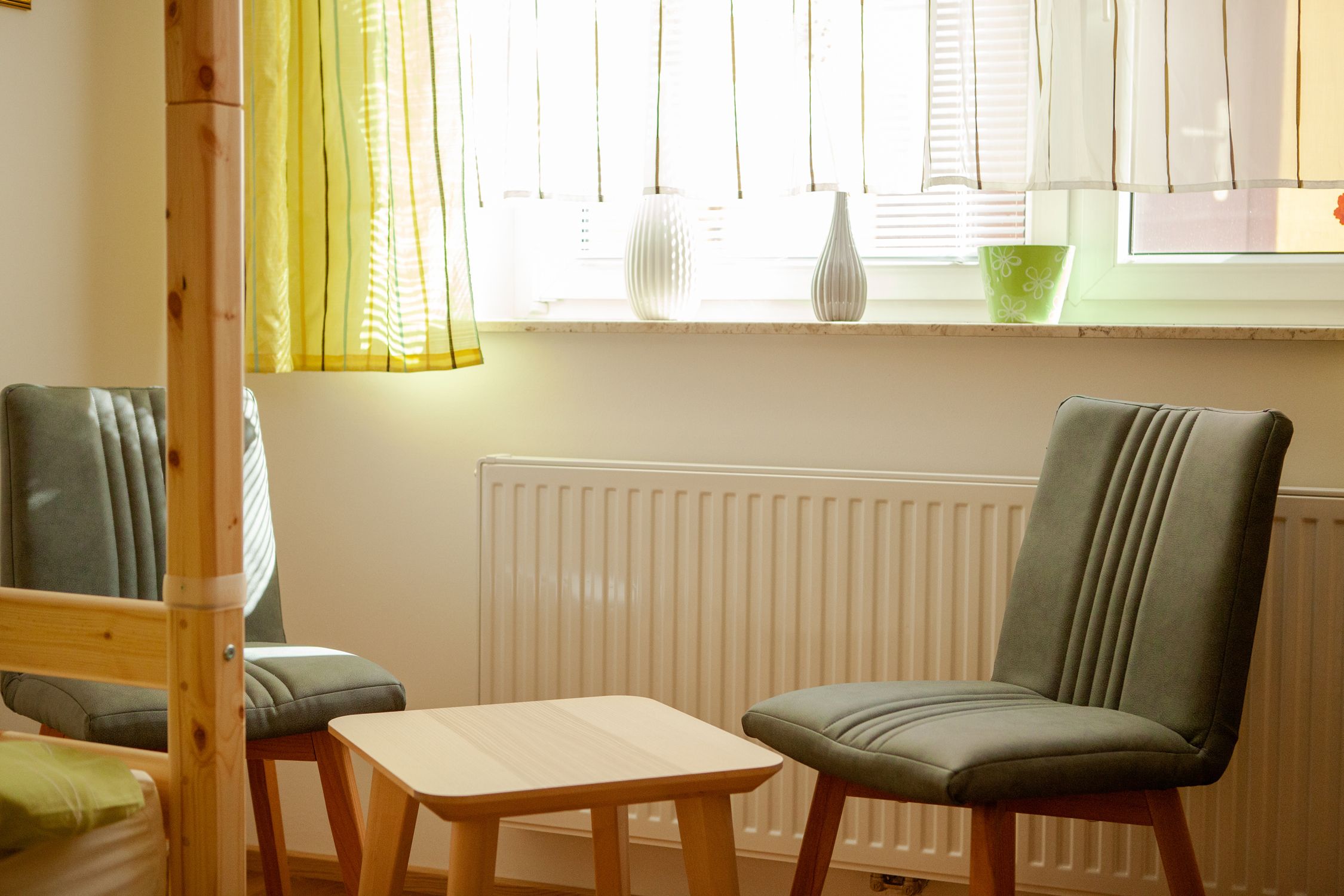 Zwei graue Stühle und ein kleiner Holztisch vor einem Fenster mit Vorhängen im Schlafzimmer.