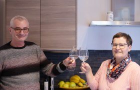 Zwei Personen sto&szlig;en mit Weingl&auml;sern in einer K&uuml;che an.