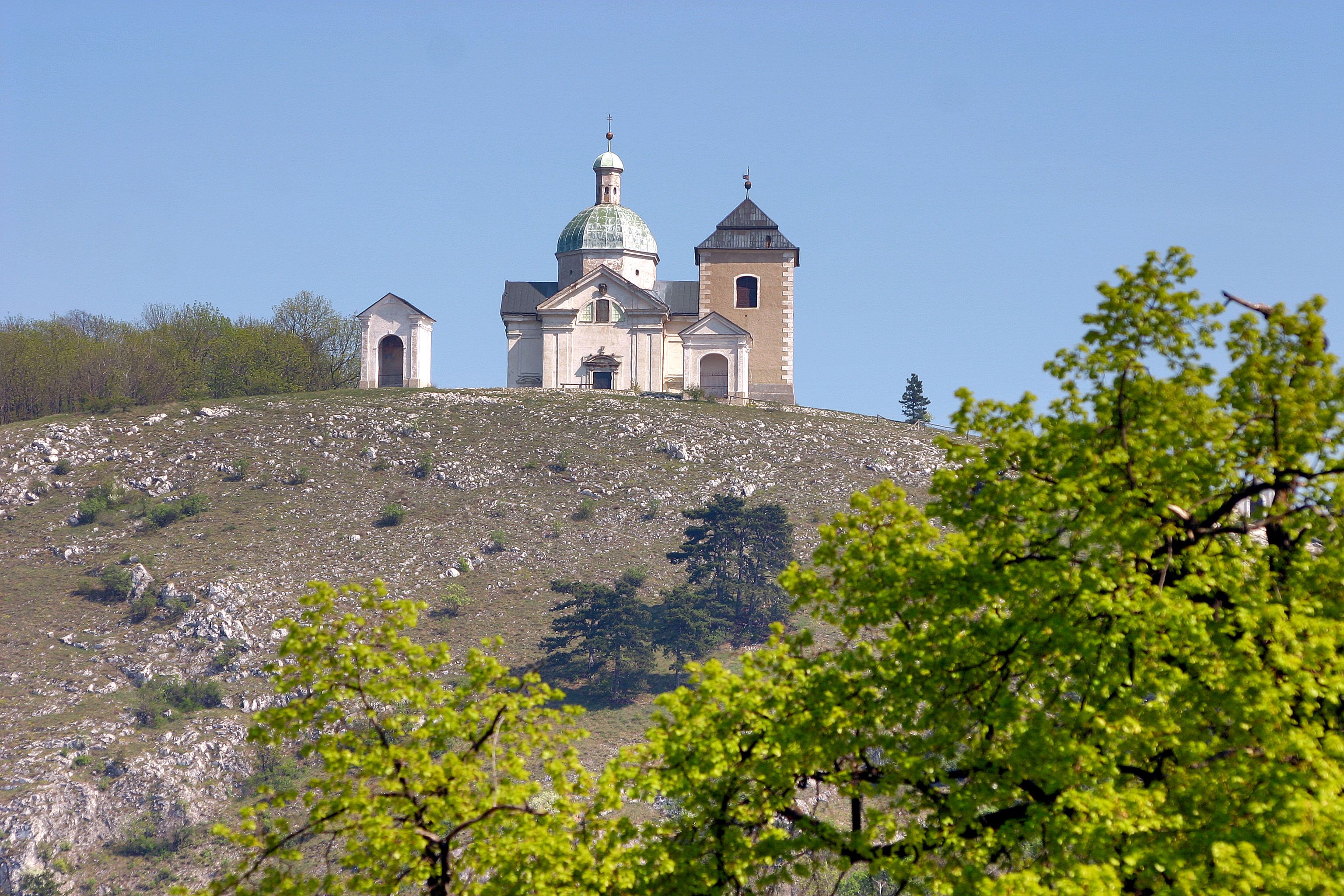 Kirche auf einem Hügel mit Bäumen im Vordergrund.