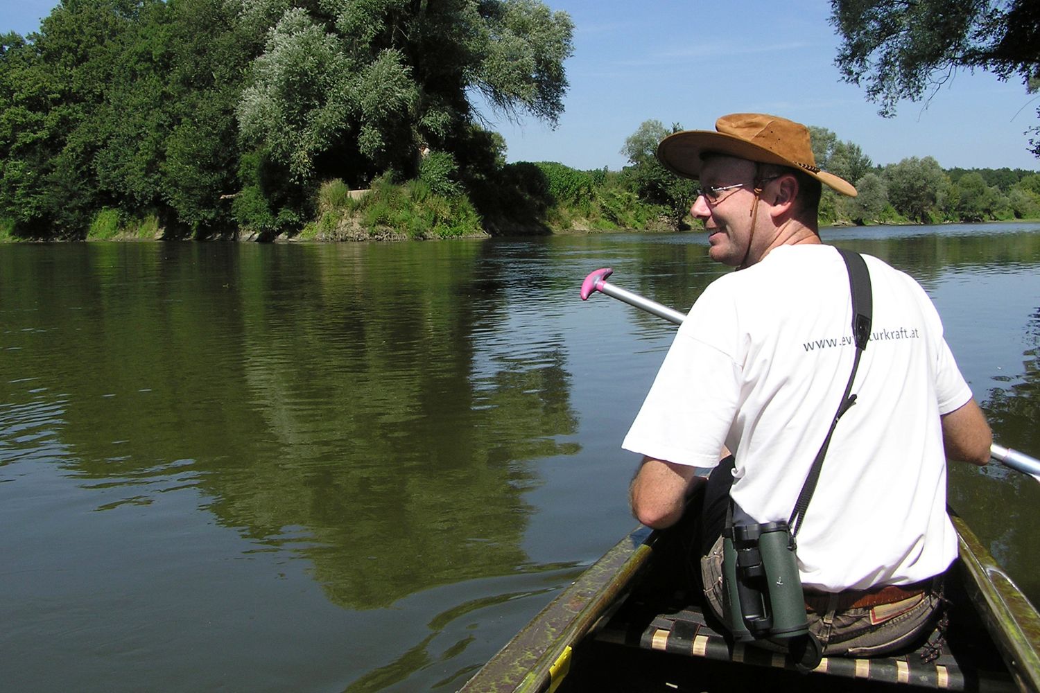Person im Kanu auf einem Fluss, umgeben von Bäumen.