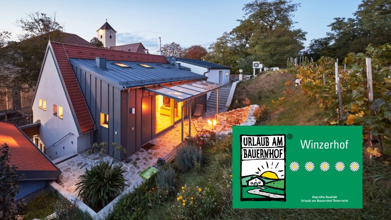 Ein modernes Kellerstöckl im Weinviertel bei Dämmerung, umgeben von Weinreben und einem Garten. Ein Schild zeigt 'Urlaub am Bauernhof'.