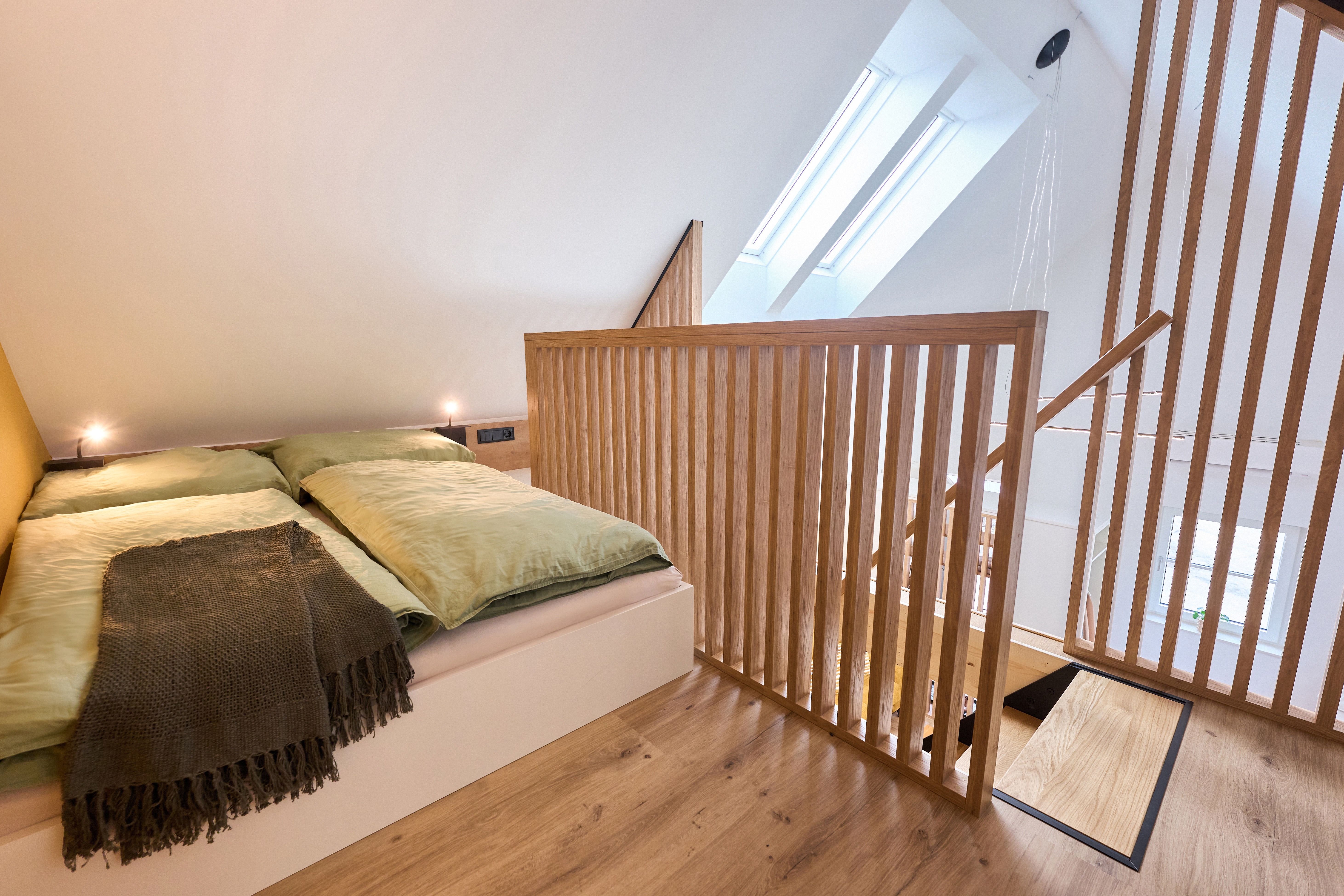 Modernes Schlafzimmer im Dachgeschoss mit Holzgeländer und Dachfenstern.