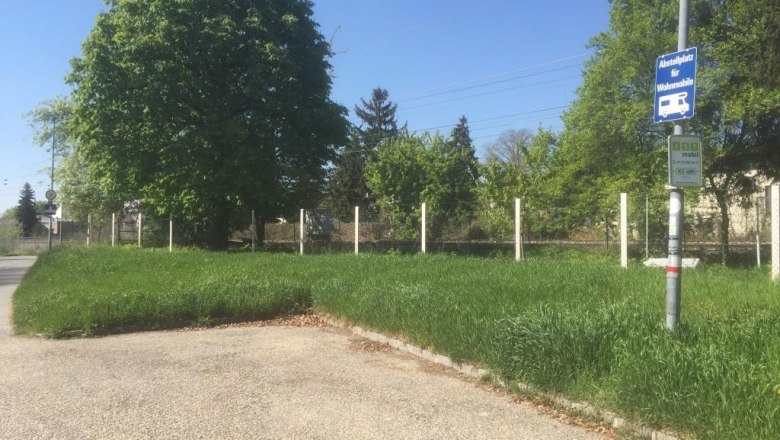 Wohnmobilstellplatz mit Schild, umgeben von Bäumen und Gras.