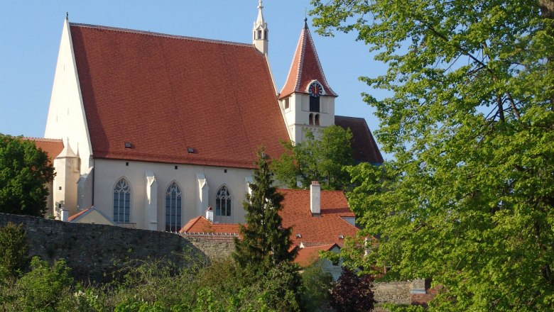 St. Stephen's parish church with red roof and tower, surrounded by trees and a stone wall.