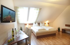 Ein gemütliches Gästezimmer mit Doppelbett, Flachbildfernseher, Tisch mit Stühlen und Dachfenstern.