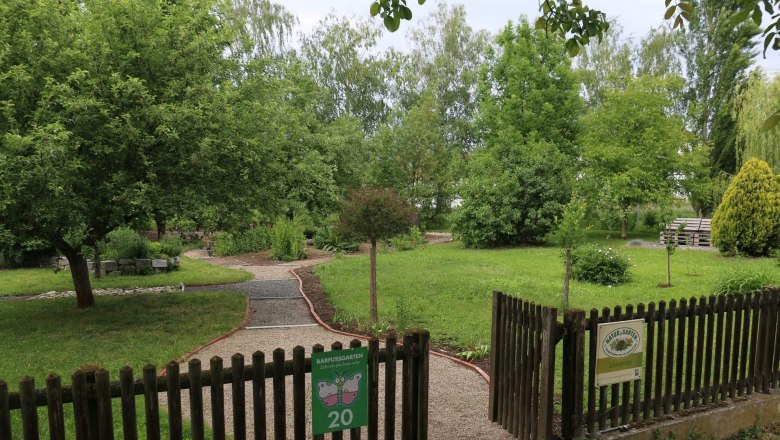 Eingang zu einem Barfußgarten mit Kiesweg und grüner Umgebung.