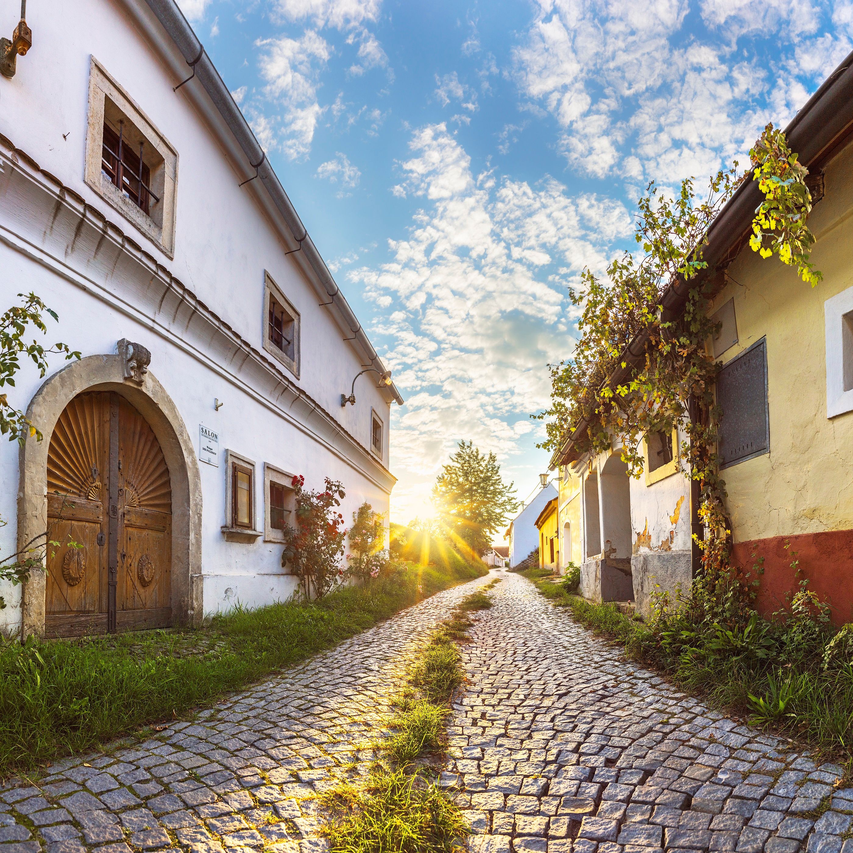 Kopfsteinpflasterstraße in Röschitz mit historischen Gebäuden und Sonnenuntergang.