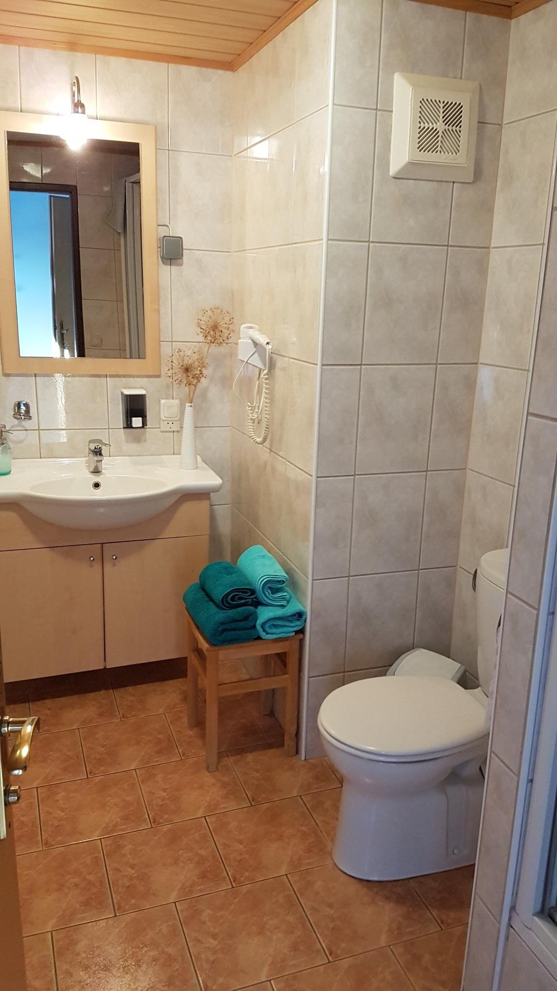 Ein Badezimmer mit Waschbecken, Spiegel, Toilette und Handtüchern auf einem Hocker.