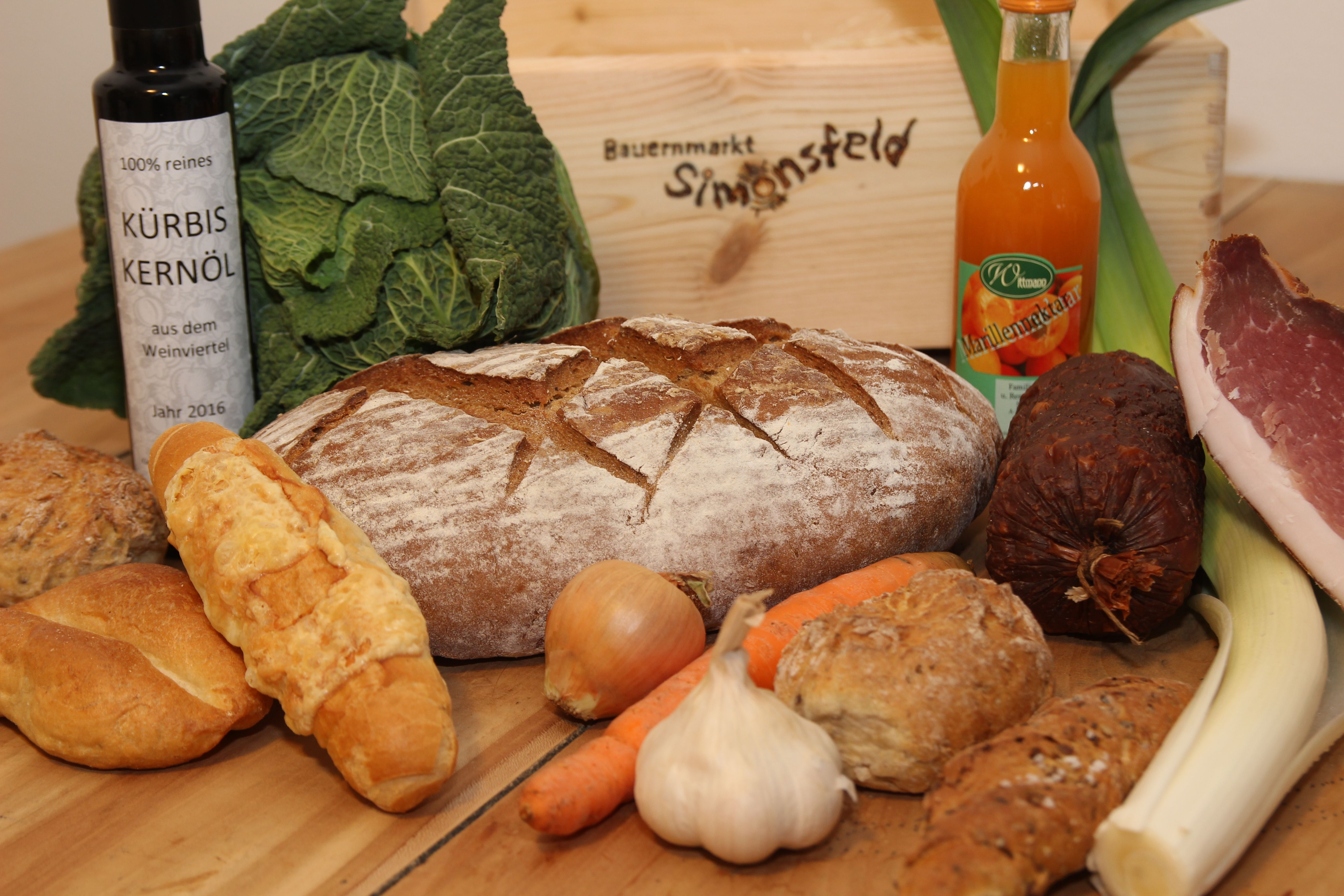 Verschiedene Lebensmittel wie Brot, Gemüse, Öl und Wurst auf einem Tisch.