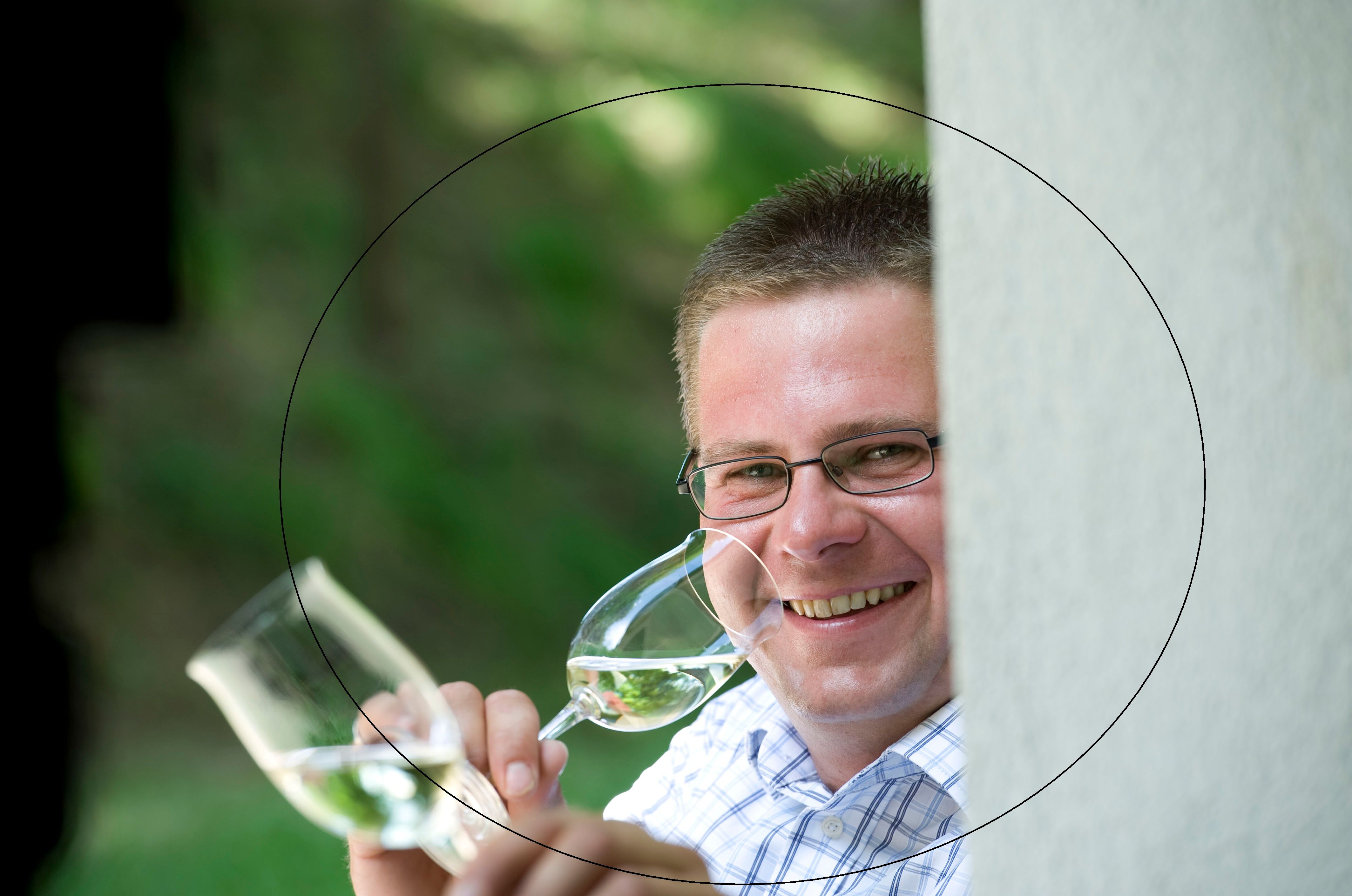 Man with glasses holds two glasses of wine and smiles.