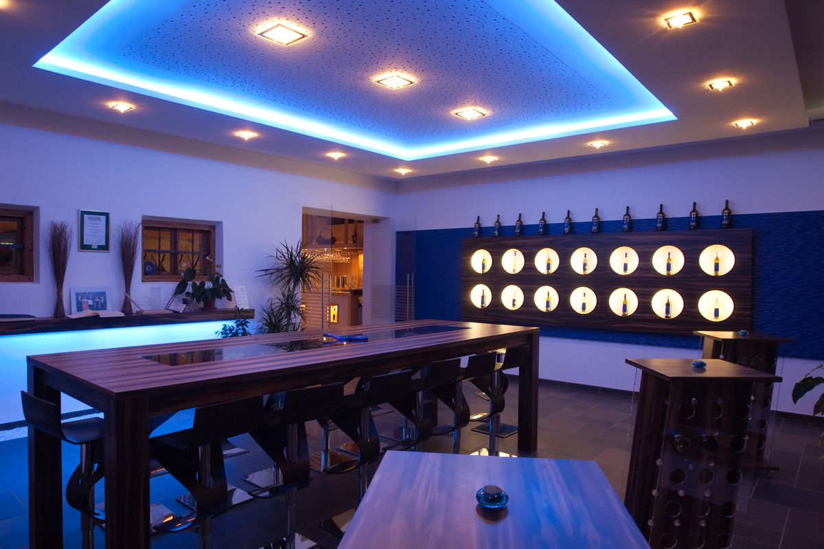 Modern tasting room with blue lighting, wooden tables and wine bottles on the wall.