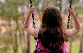 Ein Kind schaukelt auf einer Schaukel im Freien, umgeben von Bäumen.