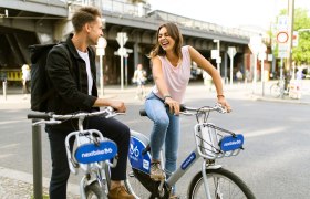 Zwei Personen auf Nextbike-Fahrrädern in einer Stadt, lachend und sich unterhaltend.