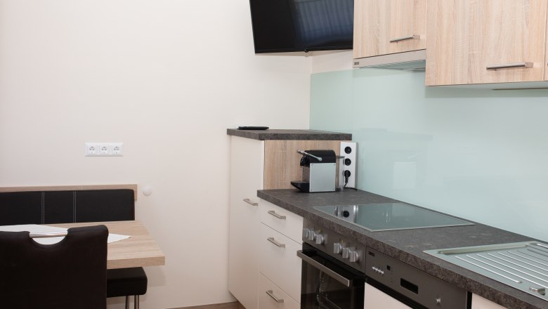 Moderne K&uuml;che mit Herd, Sp&uuml;le, Kaffeemaschine und Wandfernseher.