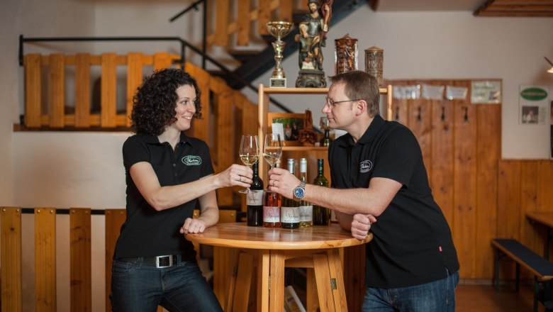 Two people clink glasses of wine at a wooden table.