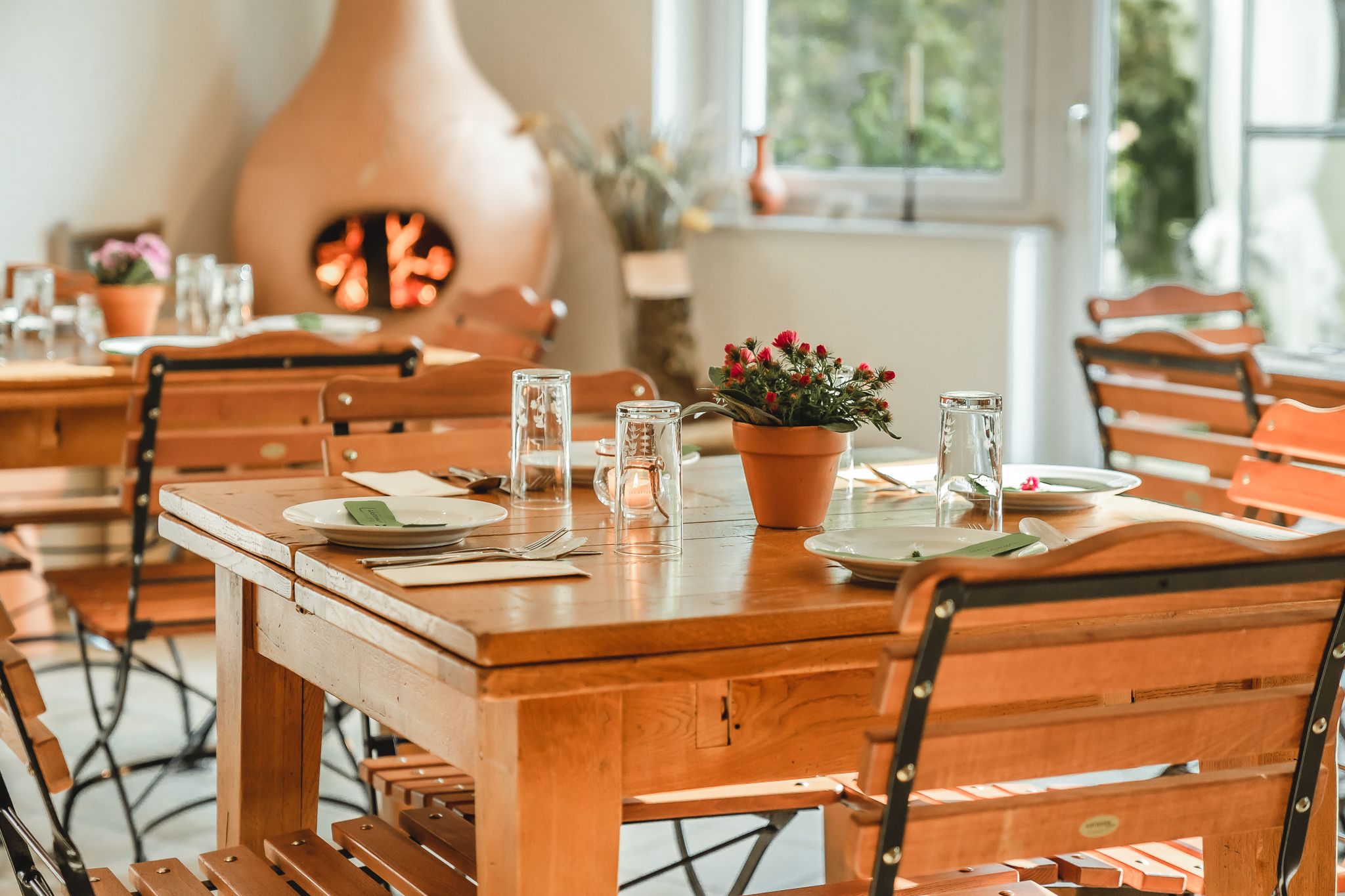 A cozy breakfast room with wooden tables and chairs, set with crockery and glasses. A fireplace in the background creates a warm atmosphere.