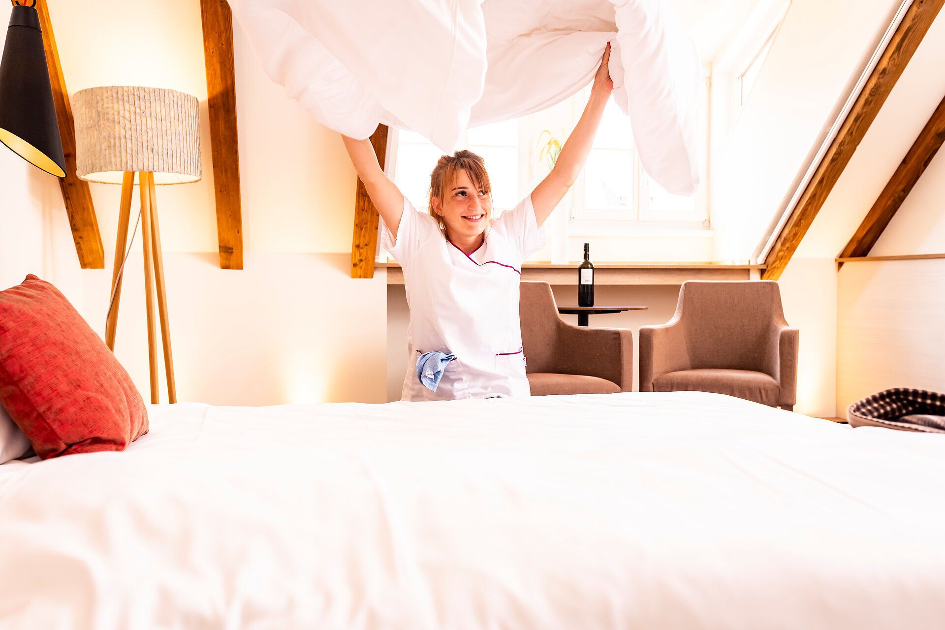 In einem einladenden Zimmer wird mit einem frischen Bettbezug eine gemütliche Atmosphäre geschaffen. Die warmen Holztöne und das sanfte Licht laden dazu ein, sich zu entspannen und die Ruhe zu genießen. Hier findet jeder Gast den perfekten Rückzugsort nach einem erlebnisreichen Tag.
