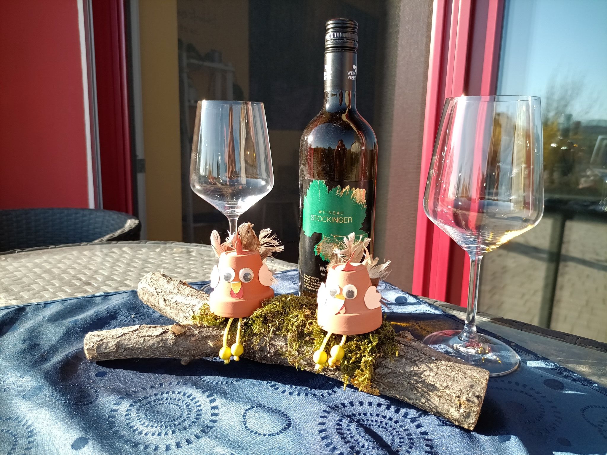 Weinflasche mit zwei leeren Gläsern und dekorativen Figuren auf einem Tisch.