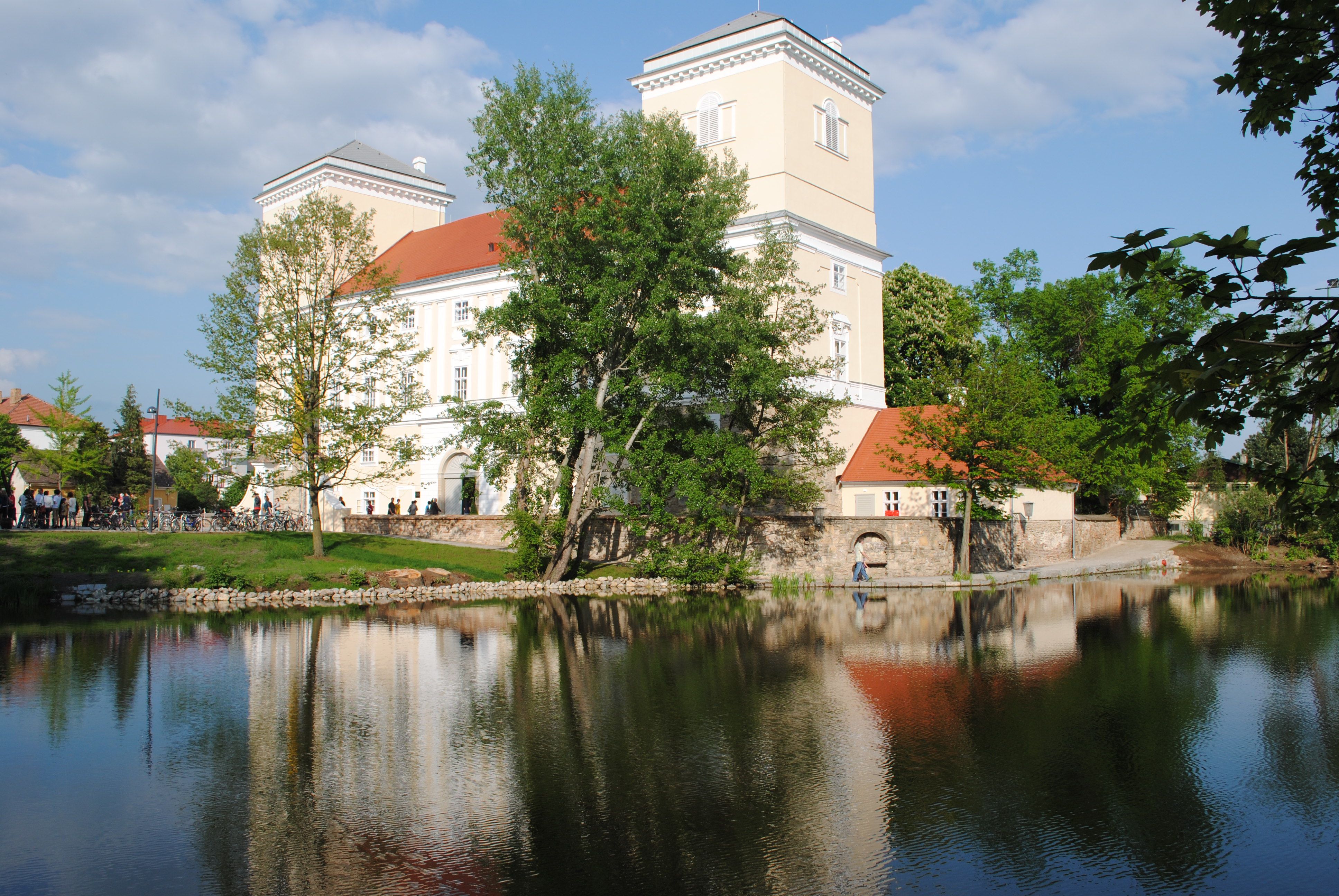 Schloss Wolkersdorf mit Teich im Vordergrund und Bäumen im Hintergrund.