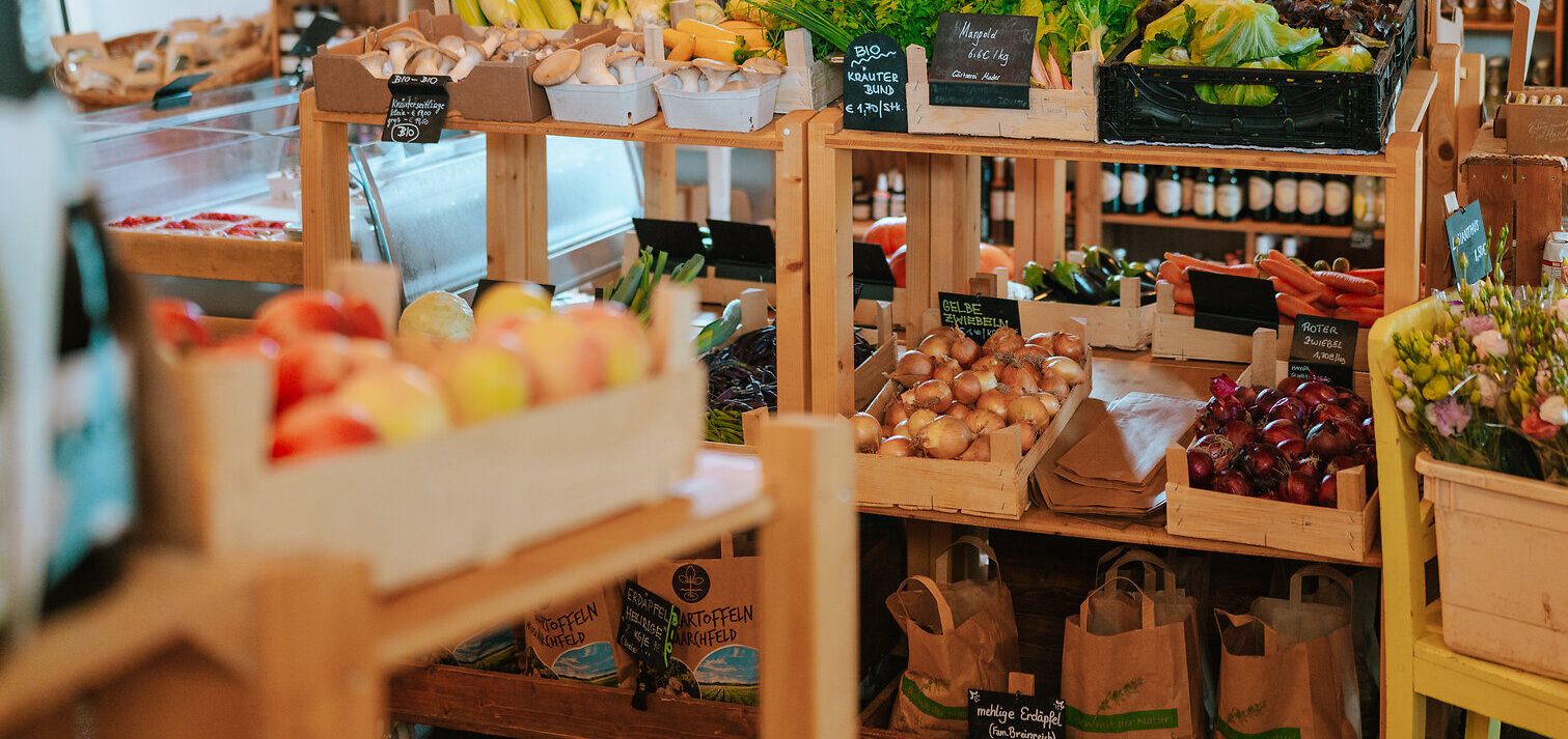 In einem einladenden Hofladen strahlen frische, bunte Gemüse und Obstsorten um die Wette. Die Regale sind liebevoll gefüllt mit regionalen Köstlichkeiten, die den Duft des Landlebens verbreiten und zum Verweilen einladen.