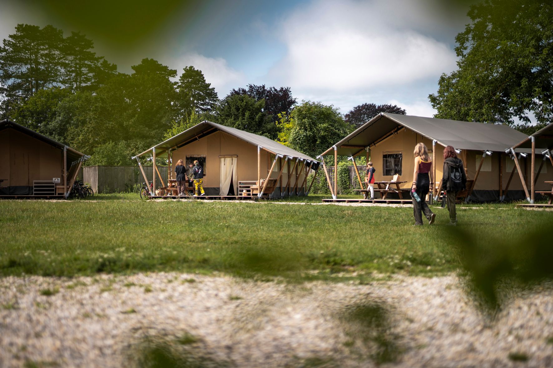 Zwei Zelte auf einer Wiese mit Menschen im Vordergrund und Bäumen im Hintergrund.