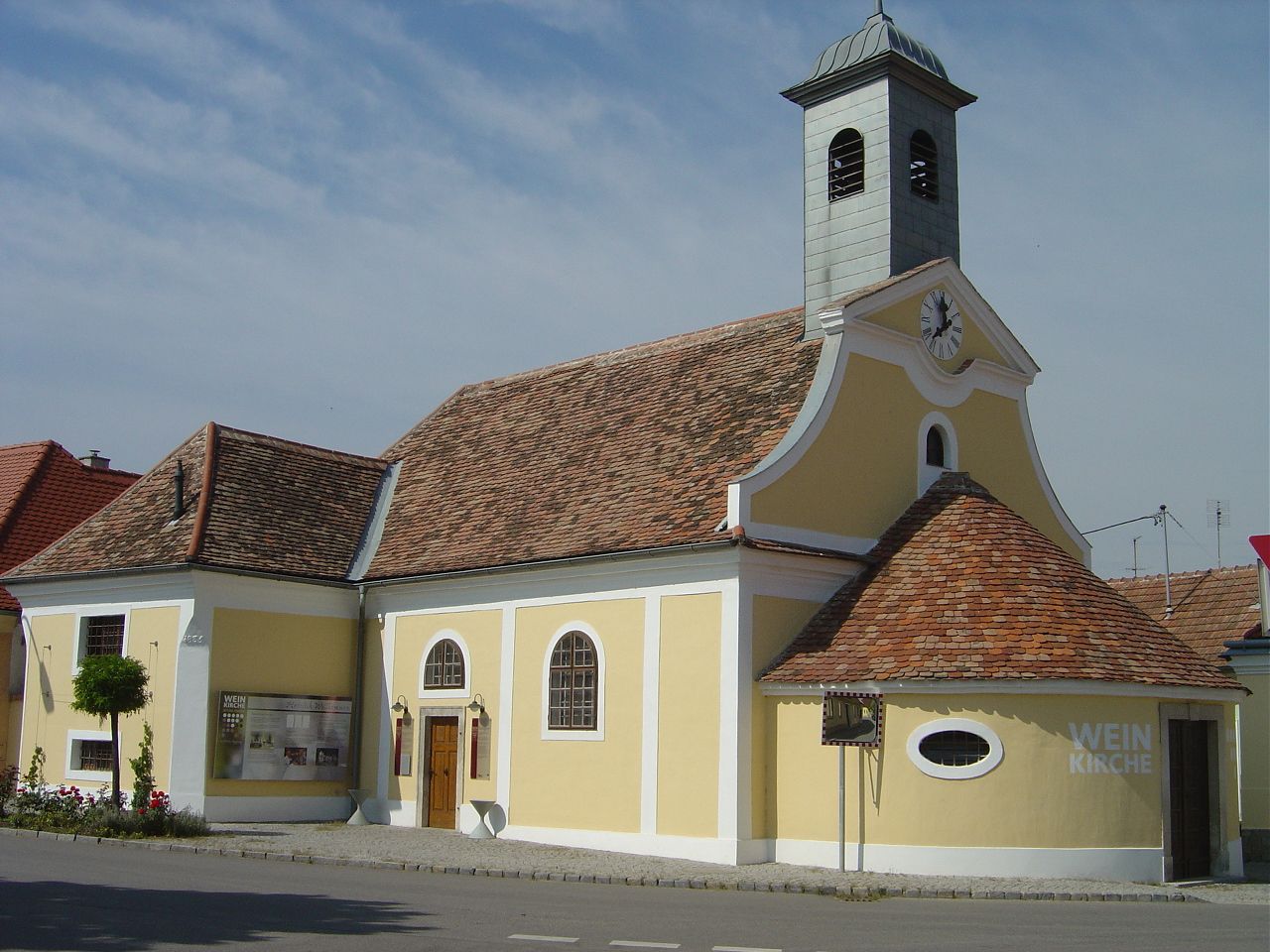 Gelbes Gebäude mit Turm und Uhr, bekannt als Weinkirche in Haugsdorf.