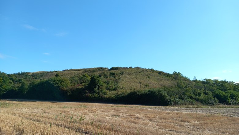 Landschaft mit Hügel und Feld unter blauem Himmel.