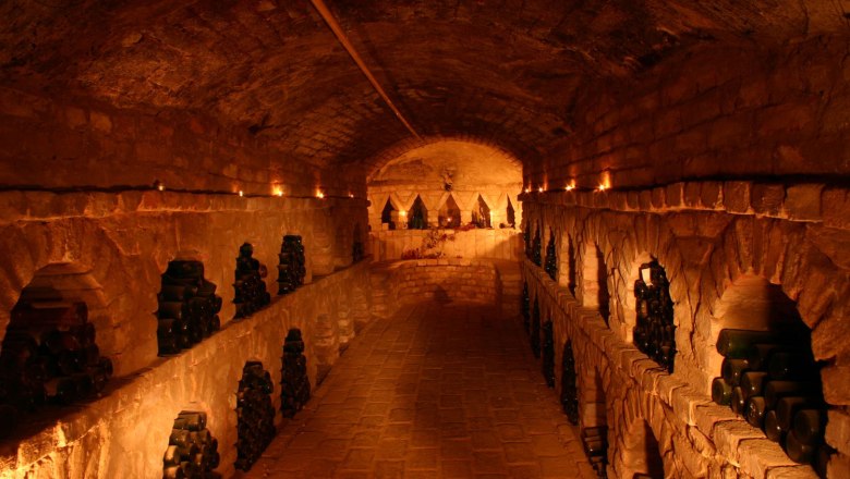 An atmospherically lit wine cellar with bottles stacked in niches along the walls.