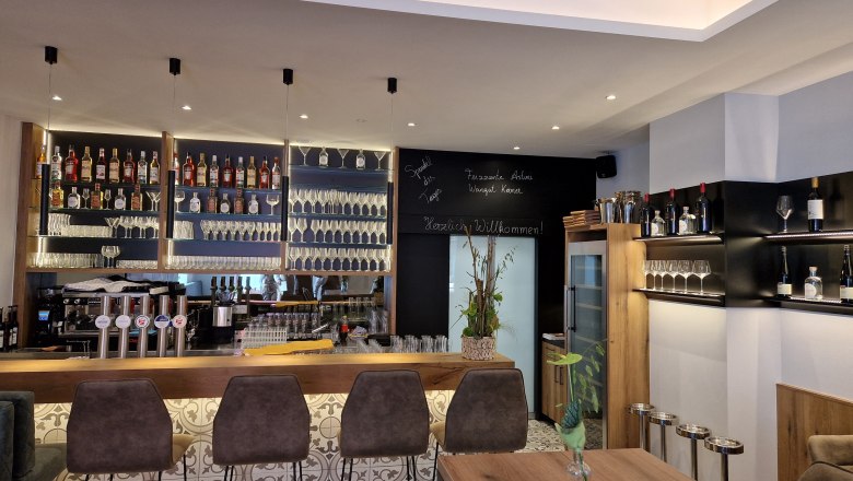 Moderne Bar mit Flaschenregalen, Gläsern und Barhockern.