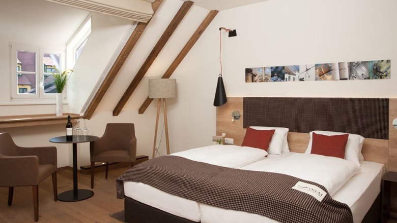 Gem&uuml;tliches Hotelzimmer mit Doppelbett, Sitzbereich und Dachschr&auml;ge.